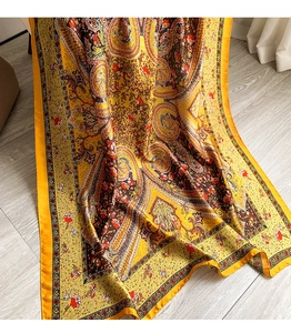 Detail view of yellow paisley floral silk scarf on light wood floor with soft lighting
