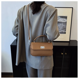 Close-up of tan leather crossbody bag with silver twist lock on gray suit outfit