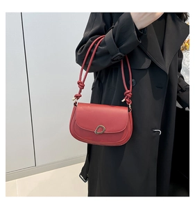 Detail of red saddle bag with gold hardware buckle and knotted shoulder strap on coat