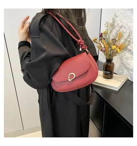 Detail of red saddle bag with gold hardware and knotted strap against minimalist decor
