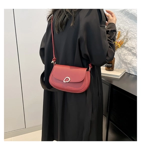 Detail of red leather saddle bag with unique gold buckle and slim shoulder strap