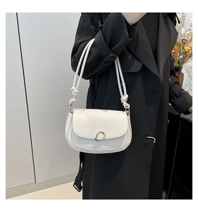 Detail of white half-moon saddle bag featuring golden metal ring and knotted strap