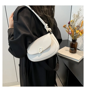 Detailed view of a white minimalist saddle bag with unique metal buckle and knot strap detail