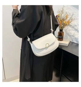 Close-up of white saddle bag with gold buckle on black coat for minimalist winter fashion