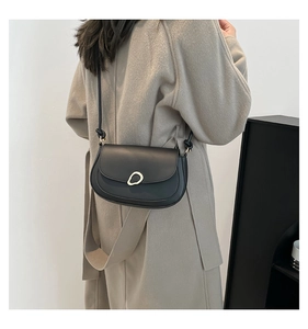 Detail of a black matte leather saddle bag featuring a stylish gold circular metal buckle