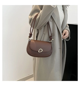 Detail of dark brown leather shoulder bag with gold metal buckle and knotted strap accents
