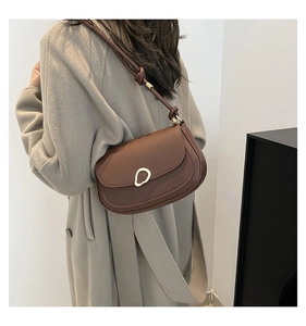 Detail of dark brown leather saddle bag with gold ring buckle on model with wool coat