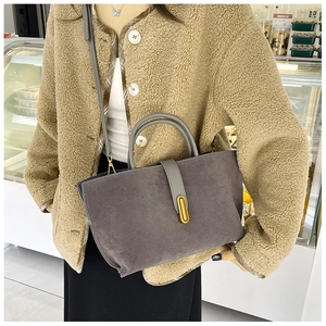 Detail view of a gray suede tote bag featuring a gold buckle and elegant top handles