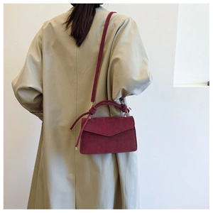 Detail of burgundy frosted leather crossbody bag with knot handle on a beige trench coat