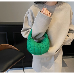 Close-up of vibrant green quilted half-moon handbag carried by a model in casual wear