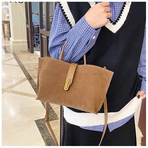Detail of a brown matte suede tote bag featuring a decorative gold oval metal buckle and strap