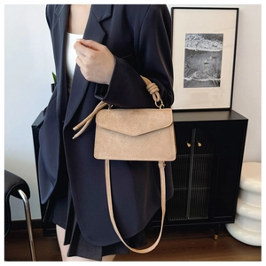 Beige matte suede crossbody bag with knot handle detail worn with a dark suit