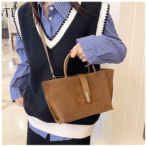 Detail of vintage brown suede tote bag with gold metal buckle shown on a shoulder