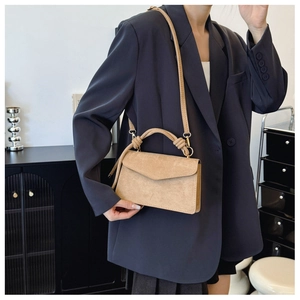 Detailed view of beige matte leather crossbody bag with knot handle on model in suit