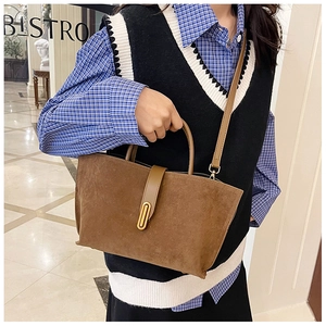 Detail of a brown suede tote bag with a golden metal clasp and smooth leather straps
