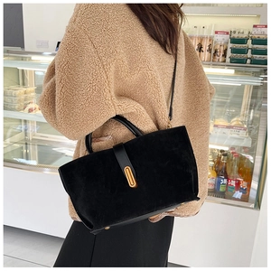Black matte tote bag with golden oval buckle shown on a model in a cafe setting