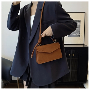 Detail of a brown suede crossbody bag showing the knot strap and gold hardware accents