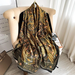 Fashionable floral paisley silk scarf in yellow and orange draped on a velvet chair