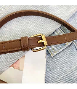 Close-up of a brown leather shoulder strap with golden metal buckle on denim fabric