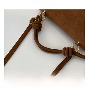 Detail of brown frosted suede texture handbag featuring a knotted handle and gold metal rings