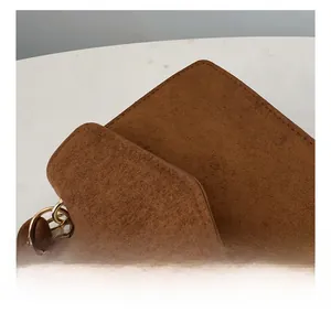 Close-up of brown suede square bag showing precise stitching and golden ring hardware