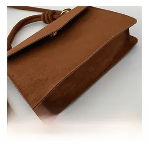Detail of caramel suede crossbody bag with gold snap closure and knotted shoulder strap