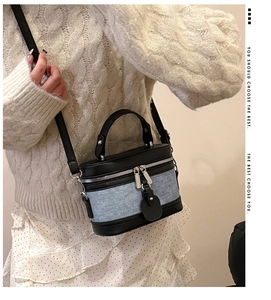 Detail of a vintage-style blue denim and black leather mini cylinder bag worn by a model