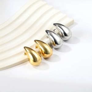 Polished gold and silver stainless steel teardrop earrings on a white wavy stone display