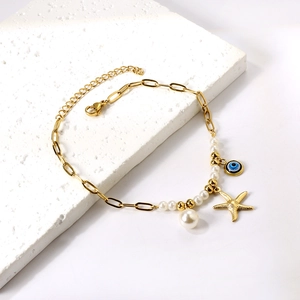 Gold starfish pearl anklet with blue evil eye charm on white textured stone background