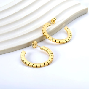 Boucles d'oreilles dorées en forme de C avec bords ciselés sur fond texturé blanc