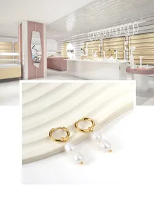 Close-up of gold hoop earrings with white pearl pendants on a white display stand