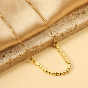Detail of gold box chain necklace featuring polished square cube beads on stone