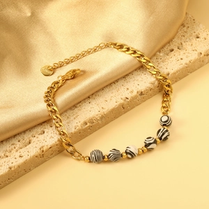 Gold stainless steel Cuban chain bracelet with zebra-striped beads on silk background