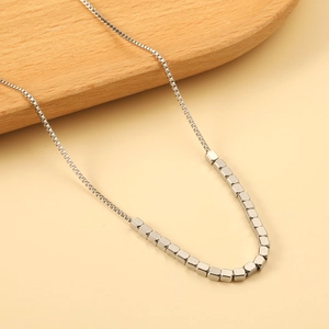 Minimalist silver steel box chain necklace featuring polished cube beads on a wooden tray