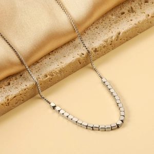 Detail of minimalist silver steel bead pendant necklace on textured stone and gold satin