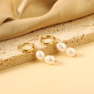 Elegant gold hoop earrings with double white baroque pearls on a beige stone surface