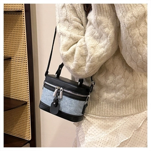 Detail of a denim and leather cylinder crossbody bag with silver double zipper and handle