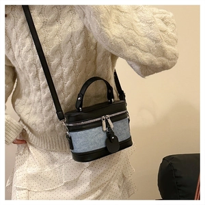 Detail of a contrast cylindrical crossbody bag in blue denim and black leather texture