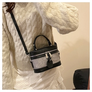 Detailed view of bicolor cylinder bag worn by model with textured fabric and leather trim
