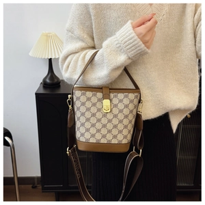 Detail of printed bucket bag with wide logo strap and gold-tone clasp on shoulder