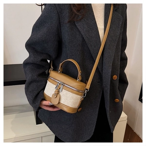 Detail of vintage canvas box bag with brown leather trim held by a model in a grey suit