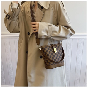 Brown printed bucket bag with wide textile strap shown on a woman in a trench coat