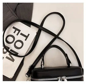 Detail of minimalist black leather crossbody bag with silver zipper and slim handle
