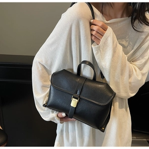 Detail of black leather handbag featuring white contrast stitching and gold square clasp