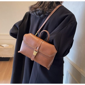 Detail view of a vintage caramel leather crossbody bag with metal buckle and top handle