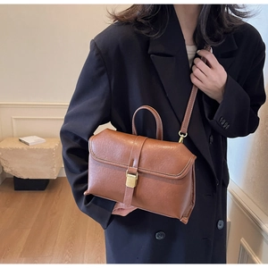 Model wearing retro brown leather crossbody bag with gold buckle over black blazer coat
