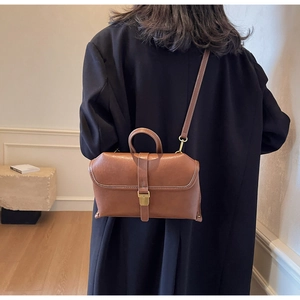 Close-up of retro brown leather crossbody bag with top handle and metallic buckle