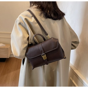 Detail of dark brown leather shoulder bag with white contrast stitching and gold buckle