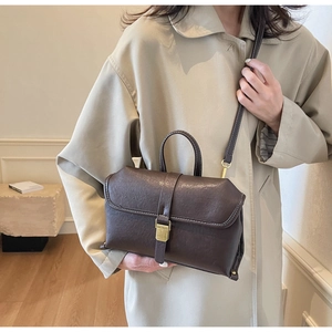 Detail of dark brown vintage leather shoulder bag with gold buckle on a beige trench coat
