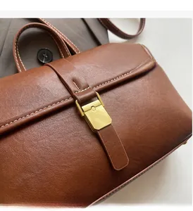 Detail of brown leather bag featuring white contrast stitching and gold rectangular buckle